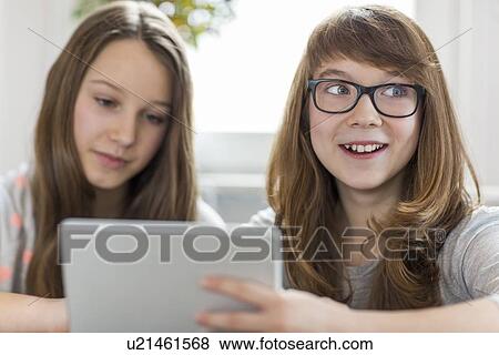 Happy girl with sister using digital tablet at home View Large Photo Image Stock Photo - Happy girl with sister using digital tablet at home. Fotosearch