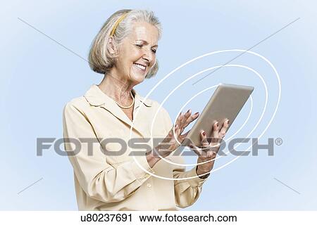 Stock Image - Happy senior businesswoman using tablet PC against clear blue sky. Fotosearch