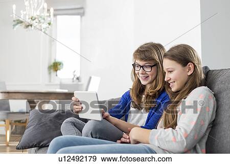 Happy sisters using digital tablet on sofa at home View Large Photo Image Stock Photo - Happy sisters using digital tablet on sofa at home. Fotosearch