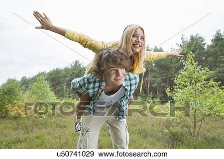 Stock Photo - Happy woman enjoying piggyback ride on man in forest. Fotosearch