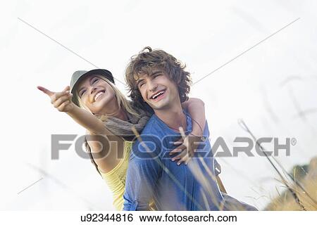 Happy woman enjoying piggyback ride on man in field View Large Photo Image Stock Photograph - Happy woman enjoying piggyback ride on man in field. Fotosearch