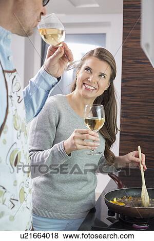 Stock Photo - Happy woman having wine with man while cooking in kitchen. Fotosearch