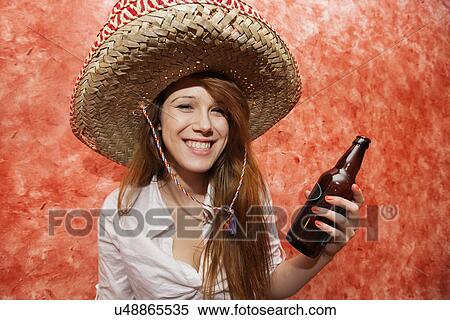 Stock Photography - Happy woman in Mexican hat holding beer bottle in restaurant. Fotosearch