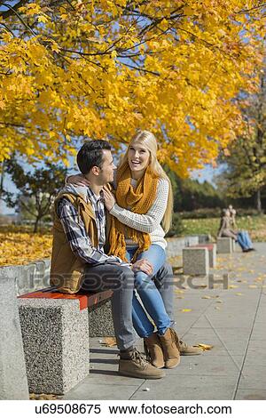 Stock Photography - Happy woman sitting on man's lap at park during autumn. Fotosearch