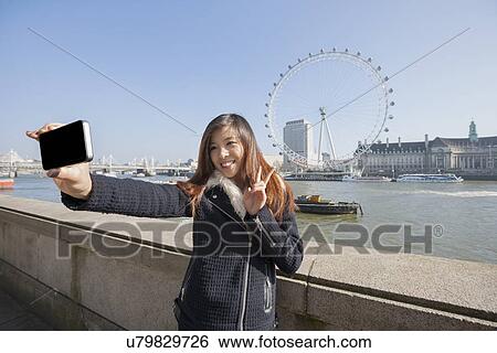 Happy woman taking self portrait through cell phone against London Eye at London, England, UK View Large Photo Image Stock Photograph - Happy woman taking self portrait through cell phone against London Eye at London, England, UK. Fotosearch