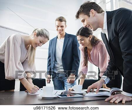 Stock Photograph - Happy young business people brainstorming at conference table. Fotosearch