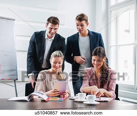 Stock Photo - Happy young business people using tablet PC at desk in office. Fotosearch