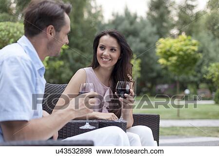 Happy young couple having red wine on chairs in park View Large Photo Image Stock Photo - Happy young couple having red wine on chairs in park. Fotosearch