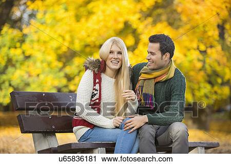 Happy young couple sitting on park bench during autumn View Large Photo Image Stock Image - Happy young couple sitting on park bench during autumn. Fotosearch