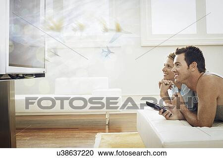 Stock Image - Happy young couple watching TV at home. Fotosearch