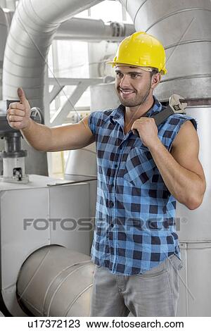 Stock Image - Happy young male worker gesturing thumbs up in industry. Fotosearch