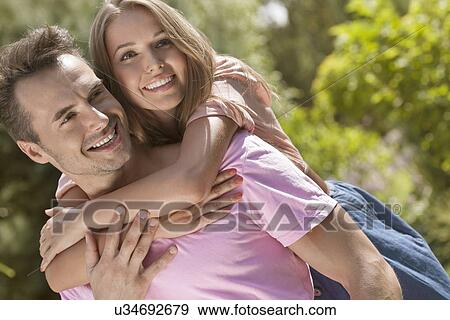 Stock Photo - Happy young man giving piggyback ride to woman in park. Fotosearch
