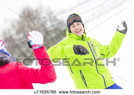Stock Photography - Happy young man throwing snowball towards woman. Fotosearch