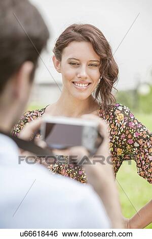 Happy young woman being photographed by man in park View Large Photo Image Stock Photograph - Happy young woman being photographed by man in park. Fotosearch