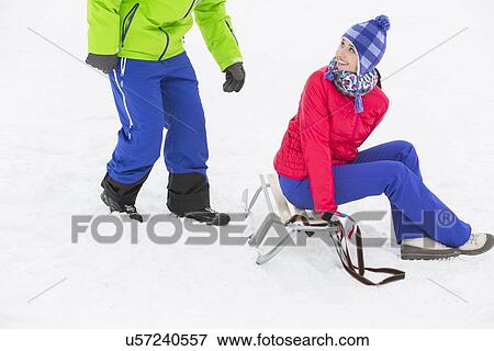 Happy young woman sitting on sled while looking at man in snow View Large Photo Image Stock Photo - Happy young woman sitting on sled while looking at man in snow. Fotosearch