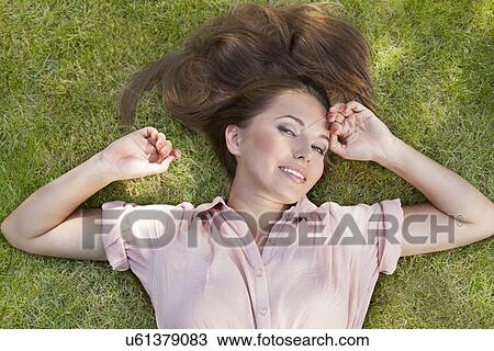 Stock Image - High angle portrait of beautiful young woman lying in grass. Fotosearch