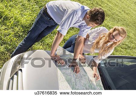 High angle view of couple reading map on car hood during road trip View Large Photo Image Stock Photography - High angle view of couple reading map on car hood during road trip. Fotosearch