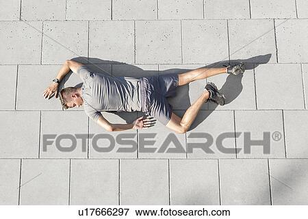 High angle view of tired sporty man lying on tiled sidewalk View Large Photo Image Stock Photo - High angle view of tired sporty man lying on tiled sidewalk. Fotosearch