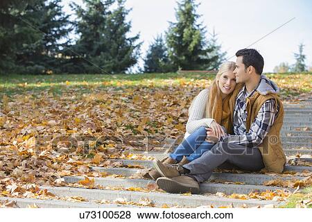 Stock Photo - Loving couple hugging while sitting on steps in park during autumn. Fotosearch