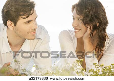 Loving couple looking at each other while lying against clear sky View Large Photo Image Stock Photograph - Loving couple looking at each other while lying against clear sky. Fotosearch
