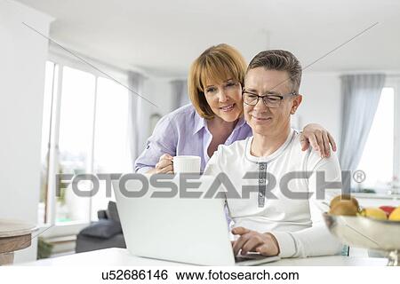 Loving couple using laptop together at home View Large Photo Image Stock Photograph - Loving couple using laptop together at home. Fotosearch