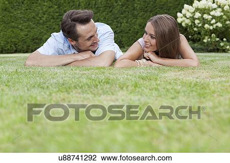 Stock Image - Loving young couple looking at each other while relaxing in park. Fotosearch