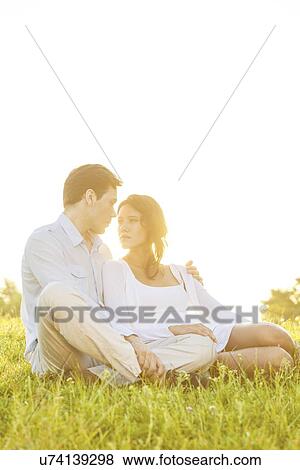 Loving young couple looking at each other on grass against clear sky View Large Photo Image Stock Photo - Loving young couple looking at each other on grass against clear sky. Fotosearch