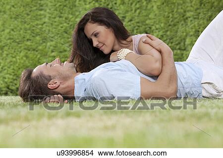 Picture - Loving young couple lying together in park. Fotosearch
