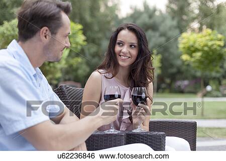 Loving young couple toasting red wine on chairs in park View Large Photo Image Stock Photograph - Loving young couple toasting red wine on chairs in park. Fotosearch