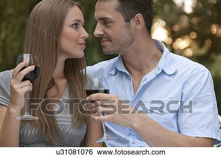 Loving young couple with red wine looking at each other in park View Large Photo Image Stock Photograph - Loving young couple with red wine looking at each other in park. Fotosearch