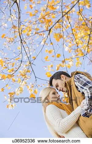 Stock Photograph - Low angle view of couple hugging against autumn tree. Fotosearch