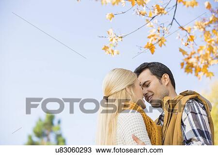 Stock Image - Low angle view of couple kissing against clear sky during autumn. Fotosearch