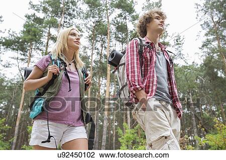 Stock Image - Low angle view of hiking couple looking away in forest. Fotosearch