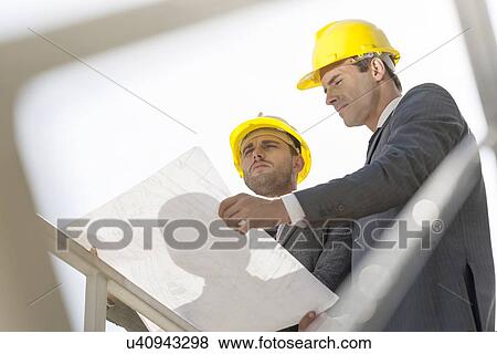 Low angle view of young businessmen holding blueprint against clear sky View Large Photo Image Stock Photo - Low angle view of young businessmen holding blueprint against clear sky. Fotosearch