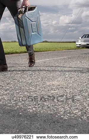 Low section of businessman carrying gasoline can with broken car in background at countryside View Large Photo Image Stock Image - Low section of businessman carrying gasoline can with broken car in background at countryside. Fotosearch