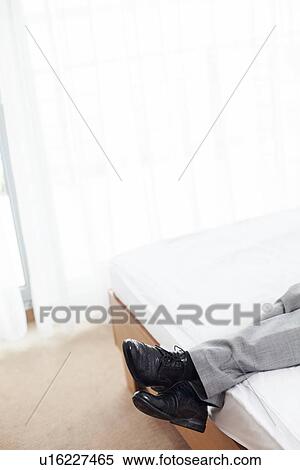 Stock Photography - Low section of businessman lying in hotel room. Fotosearch