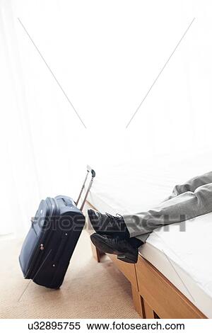 Low section of businessman relaxing on bed by luggage in hotel room View Large Photo Image Stock Photography - Low section of businessman relaxing on bed by luggage in hotel room. Fotosearch