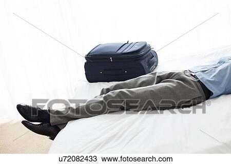 Low section of businessman sleeping beside luggage in hotel room View Large Photo Image Stock Image - Low section of businessman sleeping beside luggage in hotel room. Fotosearch