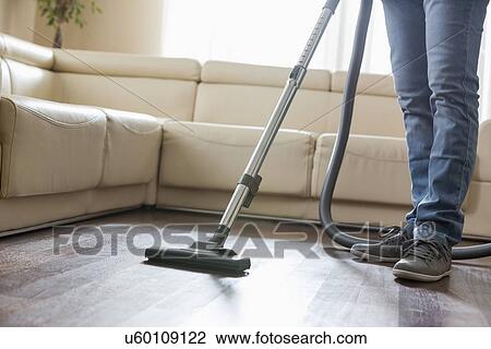 Stock Image - Low section of man cleaning hardwood floor with vacuum cleaner. Fotosearch