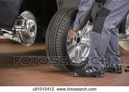 Stock Image - Low section of repairman fixing car's tire in repair shop. Fotosearch