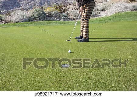 Low section of senior male golfer putting ball into hole at golf course View Large Photo Image Stock Photo - Low section of senior male golfer putting ball into hole at golf course. Fotosearch