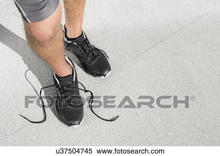 Stock Photography - Low section of sporty man with untied shoelace standing on street. Fotosearch