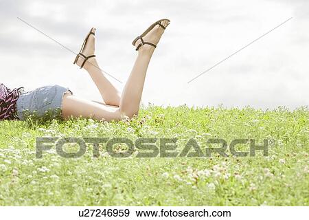 Low section of woman lying on grass against sky View Large Photo Image Stock Photo - Low section of woman lying on grass against sky. Fotosearch