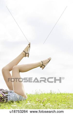 Low section of woman with feet up lying on grass against sky View Large Photo Image Picture - Low section of woman with feet up lying on grass against sky. Fotosearch