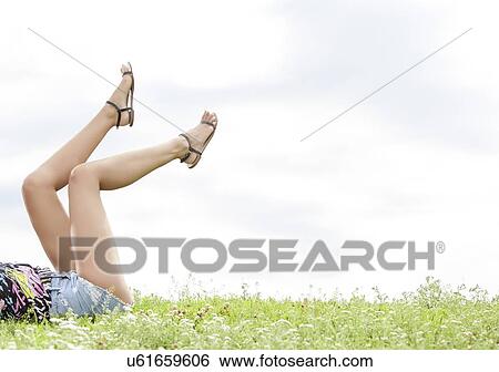Low section of woman with feet up lying on grass against sky View Large Photo Image Stock Photograph - Low section of woman with feet up lying on grass against sky. Fotosearch