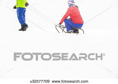 Stock Photo - Low section of young man pulling woman on sled. Fotosearch