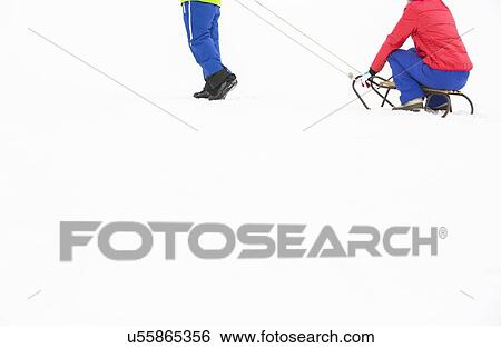 Stock Photograph - Low section of young man pulling woman on sled. Fotosearch
