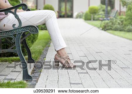 Low section of young woman sitting on park bench View Large Photo Image Stock Image - Low section of young woman sitting on park bench. Fotosearch
