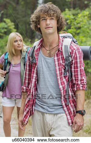 Picture - Male backpacker looking away with woman standing in background at forest. Fotosearch