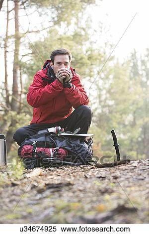 Stock Photography - Male backpacker warming hands while looking away in forest. Fotosearch